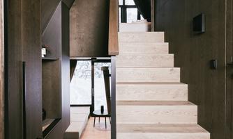 A modern entrance area with bright wooden stairs and dark walls. Large windows provide plenty of light and a view of the surroundings.