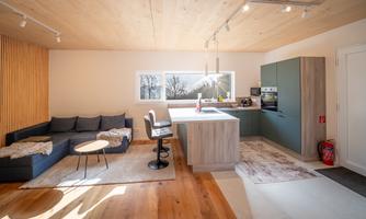 A modern kitchen with a seating area and a large window. The room features light wood and a cozy atmosphere.