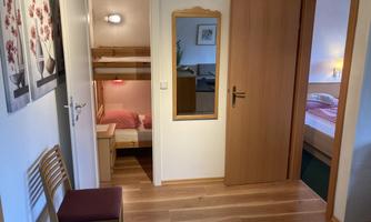 A cozy hallway with wooden floors and bright light. There are two doors to bedrooms and a mirror on the wall.