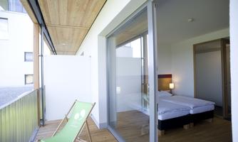 A modern room with large windows and a balcony. On the balcony, there is a deck chair and the decor is bright and inviting.