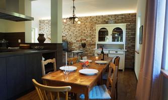 A cozy kitchen with a wooden table and chairs. The walls are clad in brick and there is a rustic cabinet.