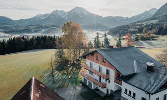 A beautiful view of a landscape with mountains and meadows. In the foreground, there is a typical Austrian building, surrounded by nature.