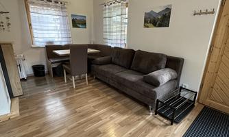 An inviting living room with a comfortable sofa and a dining area. Large windows provide plenty of daylight and a cozy atmosphere.