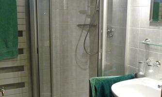 A bathroom with a modern shower cabin and a sink. Green towels are hanging on the shower cabin and on the sink.