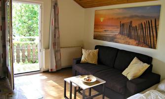 A bright living room with a sofa and a table is the centerpiece. Through the open door, you can see a small balcony and a beautiful view of the greenery.