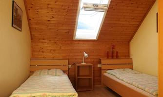 A cozy room with two single beds and wood paneling. A skylight lets in daylight and creates a bright atmosphere.