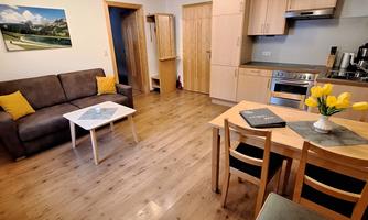 A cozy living space with a sofa, a table, and modern kitchen furniture. The atmosphere is bright and welcoming.