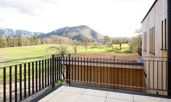 A balcony overlooking a green meadow and gentle hills. In the background, mountains and a blue sky can be seen.