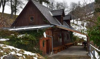A cozy wooden house in a snowy landscape. Surrounded by trees and gentle hills, it radiates rural charm.