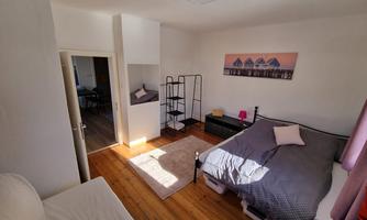 A cozy bedroom with a double bed and a window that lets in light. In the room, there is a shelf and a rug.