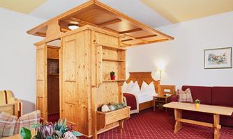 A cozy room with wooden furniture and a clear layout. There is a seating area as well as a bed in the background.