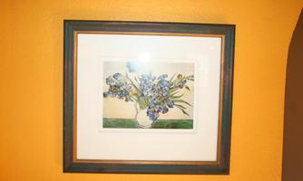 A painting with a bouquet of flowers in a vase. The flowers are depicted in various shades of blue and green, and the frame is dark green.