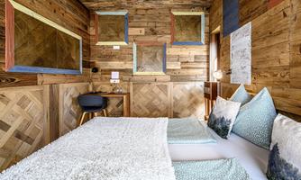 A cozy room with wooden paneling and colorful frames on the walls. The bed is furnished with decorative pillows and a soft blanket.