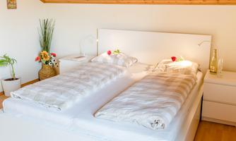 A bright room with a double bed and fresh flowers on the nightstand. The walls are painted in warm tones, and the room feels inviting.
