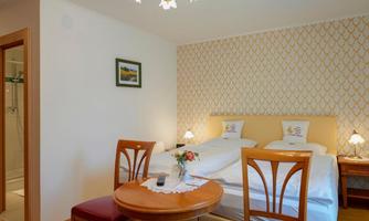 A cozy bedroom with two beds and a small table. The walls are decorated with an elegant pattern and there is a shower in the background.