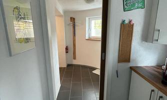 A modern entrance area with tiled flooring and an open passage to another room. On the wall hangs a sign and a bulletin board.