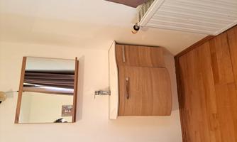 A modern wooden sink with a mirror above it. The room has wooden flooring and a heater next to the sink.