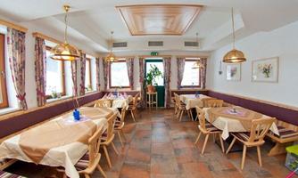 A cozy restaurant with wooden tables and chairs. The walls are light and equipped with windows and decorative curtains.
