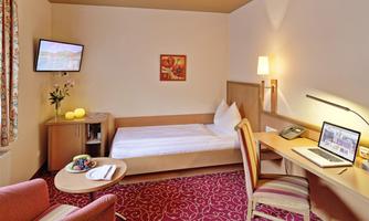 A cozy hotel room with a single bed and a desk. A TV and a small seating area complete the furnishings.
