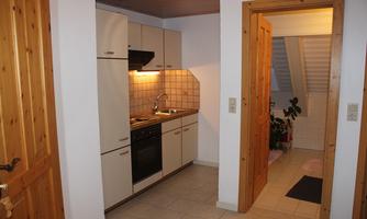 A simple kitchen with modern kitchen cabinets and a stove. In the background, an open door to another room can be seen.