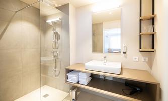 A modern bathroom with a shower and a sink. There are gray walls and a large mirror.