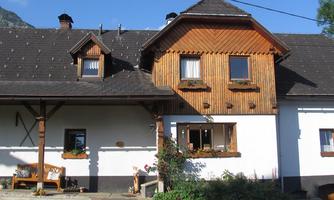 A charming house with wooden cladding and a beautiful garden. In front of the door, there is a bench and flowers in the windows.
