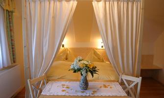 A cozy bedroom with a bed behind curtains and a small table with flowers. The atmosphere is warm and inviting.