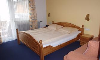 A cozy bedroom with a large wooden bed and comfortable pillows. The room has a neutral color tone and a balcony with curtains.