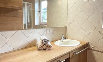 A modern bathroom with wooden shelves and a vanity. Clean towels are ready, and a large mirror reflects the space.