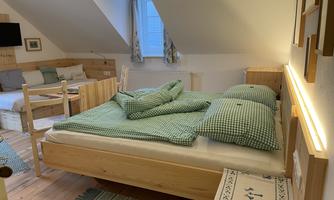 A cozy bedroom with a large bed and green plaid blankets. In the background, wooden furniture and a window can be seen.
