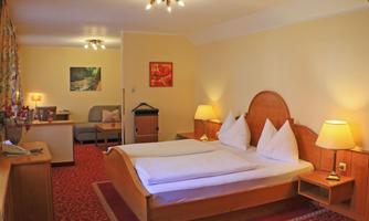 A cozy hotel room with a double bed and two nightstands. The walls are bright, and the room is equipped with a sofa and decorative pictures.