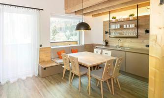 A modernly designed kitchen with a dining table and wooden chairs. The large windows provide plenty of daylight and a welcoming atmosphere.