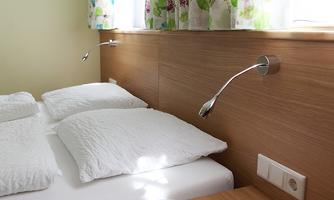 A cozy bedroom with a double bed and white pillows. The light shines through the colorful curtains, creating an inviting atmosphere.