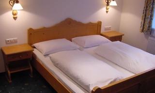 A cozy bedroom with a wooden bed and two nightstands. The walls are painted light and there is gentle lighting.