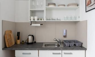 A modern, small kitchen with a sink, a kitchen unit, and shelves. Dishes and kitchen utensils are visible.