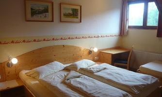 A simple bedroom with a double bed and two nightstands. A table and a chair are also available, as well as a window with natural light.