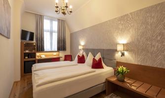 A modern hotel room with two beds and a cozy seating area. Bright colors and plenty of natural light create an inviting atmosphere.