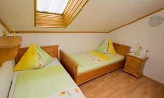 A simple bedroom with two single beds and bright bedding in green. The room has a skylight that lets in plenty of light.