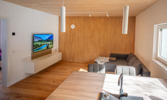 A bright living space with a modern sofa and a large television on the wall. The wooden details and the light create a warm atmosphere.