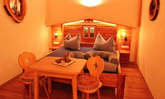 A cozy room with wooden furniture and relaxing lighting. There is a bed with large pillows and a small table with two chairs.