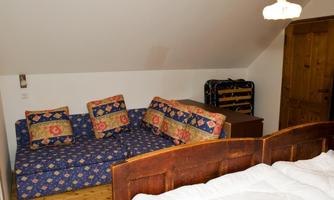 A cozy room with a blue sofa and decorative cushions. In the background, there is a wooden wardrobe and a bed.