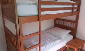 A loft bed made of wood with an upper and a lower sleeping area. Next to it, there is a small nightstand.