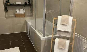 A modern bathroom with a shower and a bathtub. Clean towels are placed on a wooden rack.