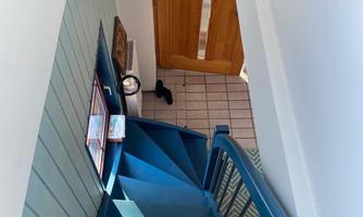 A blue staircase leads to an entrance with a wooden door. A decoration hangs on the wall, and a small toy is on the staircase.