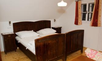 A cozy bedroom with a wooden bed and two nightstands. The walls are light, and there is a window with colorful curtains.