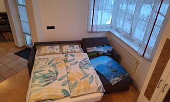 A cozy room with a sofa bed and colorful blankets. Bright curtains hang at the windows and there is a beautiful view outside.