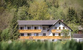 A cozy building with balconies, surrounded by green trees and hills. The tranquil landscape conveys a sense of idyll and a connection to nature.