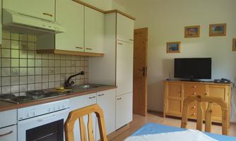A bright kitchen with modern furniture and a dining area. On the opposite side is a TV and a chest of drawers.