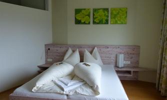 A modern bedroom with a large bed and white pillows. Three green pictures hang on the wall.