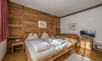 A cozy bedroom with wood paneling and two single beds. The room features a television and lovely decorations on the walls.